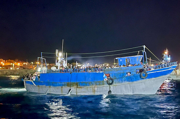 Das überfüllte blaue Fischerboot aus dem vorherigen Post bei der nächtlichen Einfahrt in den Hafen von Lampedusa.