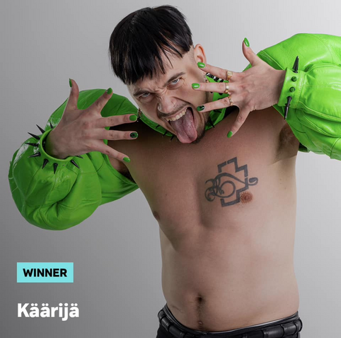 A portrait of Käärijä, a whirtless white man with dark hair wearing bright green sleeves and bright green nails. He is sticking his tongue out.