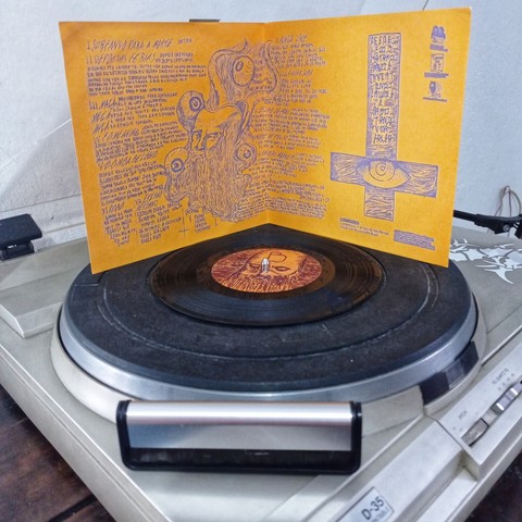 Capa do vinil aberta mostrando a parte interna e o vinil no toca discos com uma escova de limpeza na frente.