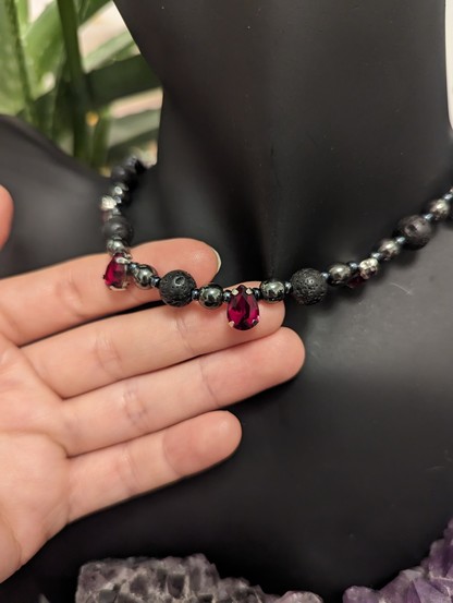 Hand showing handmade necklace with grey black beads and glass red drop pendants on a black doll