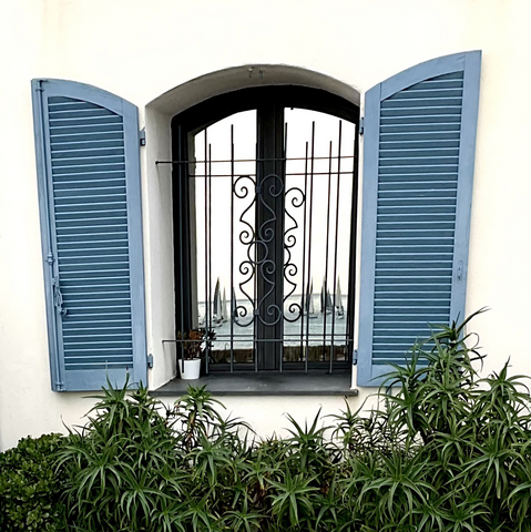 Reflection of sailboats on Antibes waterfront in window with blue shutters. 