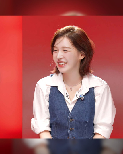 promo poster for red velvet wendy's appearance on the 'lee mujin service' show.
photo shows a portrait shot of wendy wearing a white shirt and blue vest in front of a red backdrop.
