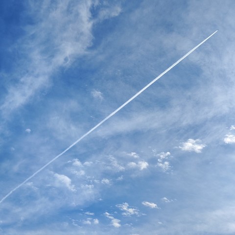 A very blue sky with wispy white clouds and the contrail from a jet which is flying diagonally across from bottom left and is about to exit top right