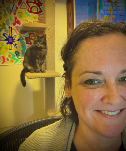 A selfie of me smiling, and my cat behind me sitting on a cat climber.