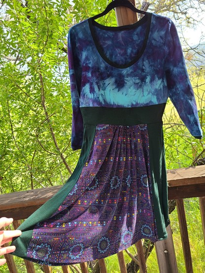 A long sleeved short dress. The skirt is forest green panels alternating with a multicolored purple/light blue/green 60's print. Top of the dress is purple tie dye over a light blue base 