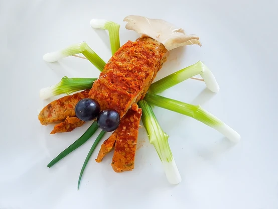 Lord of Tofu Hummer Verpackungsfoto. Ein zusammengesetzter Hummer aus einem Stück rotbraunem Tofu mit schwarzen Olivenaugen, rotbraunen Tofu Zangen, Austernpilzschwanzflosse, Knoblauchstängelbeinen und grünen Tastfühlern.