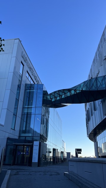 The entrance to Lilywhite House (venue for BarCamp London 12) with a twisting glass and steel bridge going across to White Hart Lane stadium,  viewed against a bright morning sky