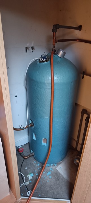A oldish copper hot water cylinder covered in blue rigid insulation foam.