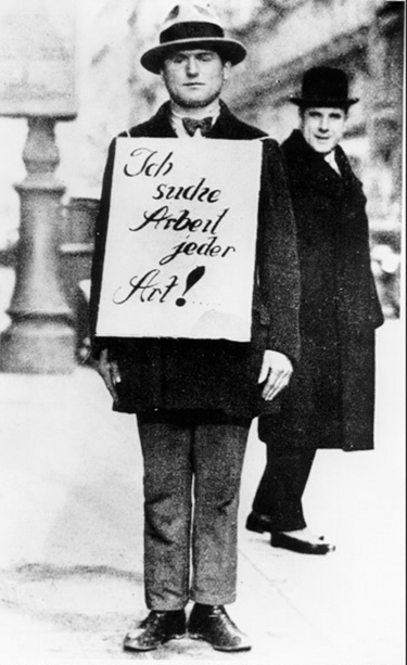 Zu sehen ist ein Foto aus der Zeit um 1930. Ein Mann trägt am Oberkörper ein Schild mit der Aufschrift "Ich suche Arbeit jeder Art".