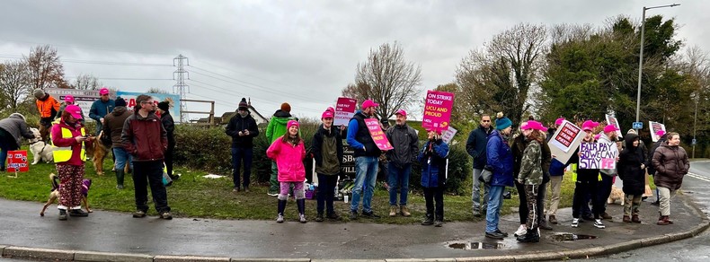 Picket line full of people in brightly coloured outdoor Big Coats and quite a lot of UCU pink caps and beanies. Lots of strike placards, including a home made one that reads "FAIR PAY SO WE CAN STAY", and loads of dogs also. Weather a bit grey but members look resolute!