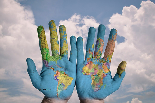 Stock image of a pair of hands painted to look like a global map set against a blue sky and cloudy background 