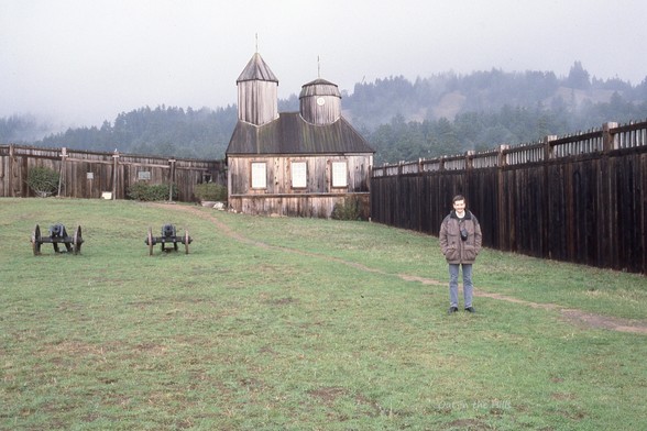 The old Russian Fort at Fort Ross California, inside a fenced area. A couple of cannons on the left and a man stood on the right.