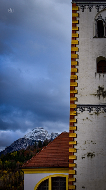 Tower of Basilica of St. Mang with Alpine peak in background against a cloudy sky, Füssen, Allgäu, Bavaria, 11 Nov 2023. Nikon D5600, Nikkor DX 35 mm ƒ1.8G, ISO 160, ƒ5.6, -0.7 ev, 1/800s