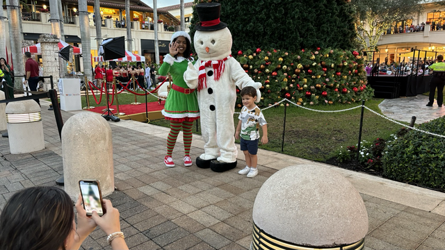 A lady elf with a snowman and a little kid as they take a picture with the mother and I.
