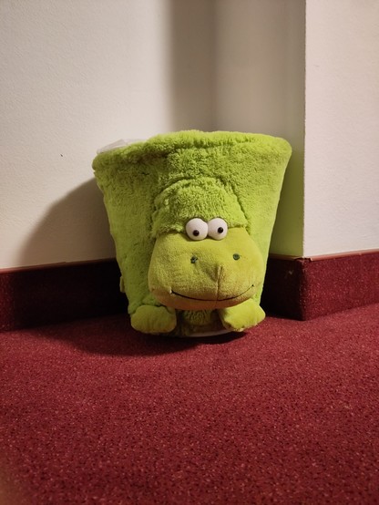 Ein Foto eines mit grünem Plüsch bezogenen Mülleimers, von der Seite gesehen. Vorne unten schauen zwei knubbelige Füße hervor. Vorne in der Mitte zwei große Kulleraugen und ein breites Maul. Insgesamt sieht das Ding aus wie ein kleines grünes Nilpferd.