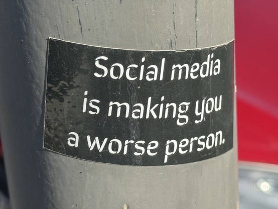 A photo of a sticker on a pole that says, “Social media is making you a worse person.”