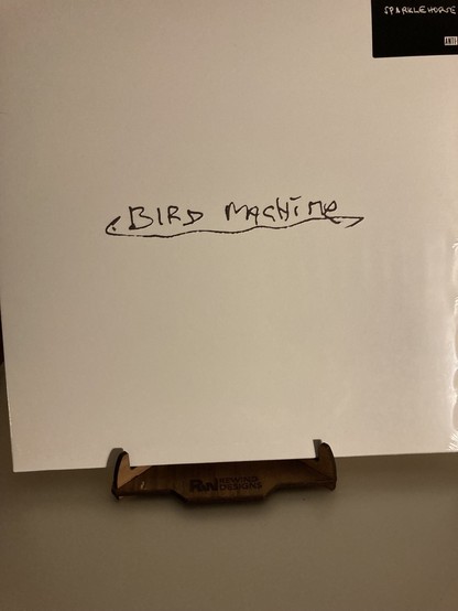 Cover of the LP Bird Machine by Sparklehorse 
Cover is a plain white background with Bird Machine written on it in silver handwriting, underlined 