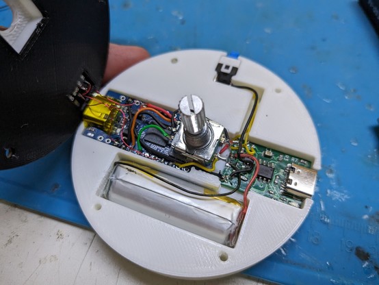 A round 3d printed enclosure showing an arduino pro micro and a charging board point to point wired up to a lipo battery and an encoder wheel