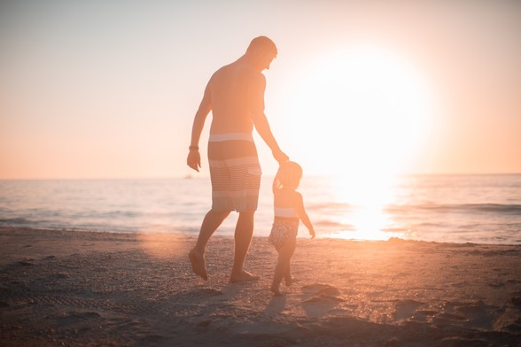 Father and daughter holding hands and walking on a beach during sunset