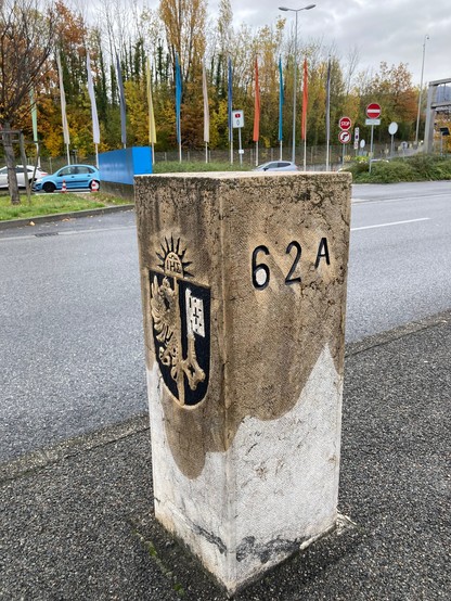 Swiss/French border stone 62A at the Bardonnex motorway border passage point, photographed close up, showing the card Geneva flag on one side.