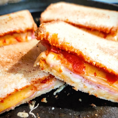 en gros plan, des croques-monsieur coupés en deux sur un plat antiadhésif. 
l'intérieur dégouline d'une pâte rouge appétissante avec le fromage fondu et le jambon, c'est de l'ajvar, une pâte de poivrons et d'aubergine. 

le sandwich est plus coloré mais également très parfumé par cette pâte. Ici c'est de l'ajvar doux mais il en existe également du piquant pour un bon kick <3 
