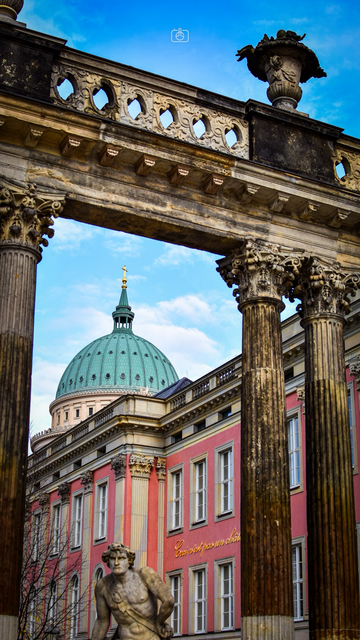 View of dome of St. Nicholas’ Church through colonnade next to the rebuilt City Palace, with the palace’s nod to Magritte «ceci n’est pas un château» visible (“this is not a palace”), Potsdam, 30 Oct 2023. Nikon D5600, Nikkor DX 35 mm ƒ1.8G, ISO 100, ƒ4, 1/250s