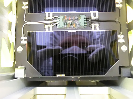 Reflection of myself in a FUNcube solar panel on the top face. A black aluminium panel with two solar cells and some wiring is visible inside a test structure