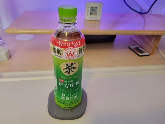 Full 500 mL plastic bottle of Japanese Suntory Lemon Cha Toshitsu Taisaku (green tea), on a gray diatomaceous-earth coaster on an off-white desk mat on a maple desk. 

The bottle has light-green cap and clear plastic covered by a mostly green label. The label background from top-to-bottom: Red (10%); gold (10%); white (5%), then light-green transitioning to dark green and then to light-green again (75%).

Japanese text and translation in English follows, from top-to-bottom.

White on red background: Wのはたらき ("How W works").

Black on gold background: 脂肪 糖質 ("Fat", "Carbohydrate")

Red 機能性表示食品 / 届出番号 E38 ("Foods with functional claims / Notification number E38") on outside border of white double circle, with Ẇ (Capital Letter W with Dot Above) at center.

Black on white, repeated under "fat" and "carbohydrate": の吸収を抑える ("suppresses the absorption of")

Black on large gold circle: 茶 ("tea").

Gold on dark-green: 機能性表示食品 ("Foods with functional claims").

White on red: 京都 ("Kyoto") followed by white on dark-green background: 福寿園 "Fukujuen".

White on dark-green: 伊右衛門 ("Lemon").

White line divider with gold outline of 3 overlapping, vertical tea leaves at center.

White on medium-green: おいしい 糖質対策 ("Delicious sugar countermeasures").

White line divider, then black on light-green: 難消化性デキストリン(食物繊維): "Indigestible dextrin (dietary fiber)".

Footer, in black on light-green: 生活は、主食、主菜、菜を基本に、食事のバランスを。("A balanced lifestyle is based on staple foods, main dishes, and vegetables.")