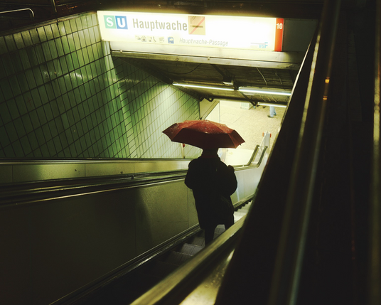 Eine Person mit Regenschirm die nachts eine Rolltreppe hinunterfährt 