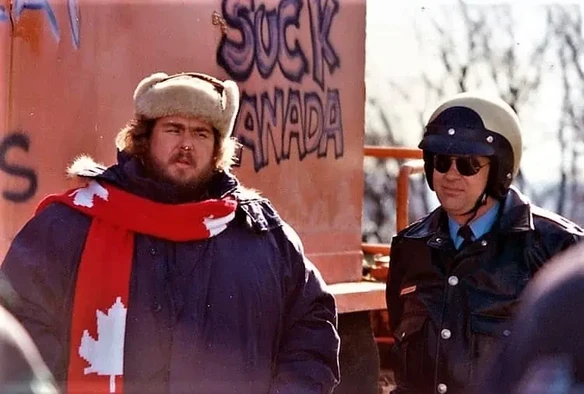 John Candy standing next to a highway patrol cop. This is a movie still from CANADIAN BACON, a satire about US-Canada relations that hinges on an imagined threat of violence from Canada in the US (at Niagara Falls, IIRC) that is sold to the public so that some of them actually believe it is happening, even though it was just made up foro political expediency. IDK, it seemed appropriate today, somehow.