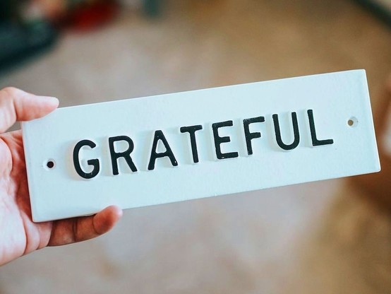 Someone holding a sign which has the text, "grateful." Shared as a reminder to take time and reflect on that which has brought joy. 