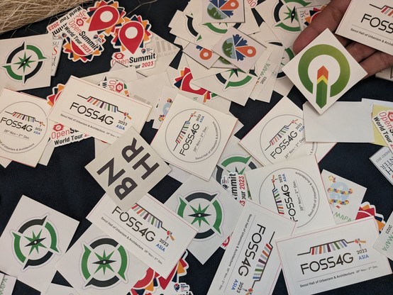 Different open geospatial swags and stickers on a table at the Pista ng Mapa 2023 conference.