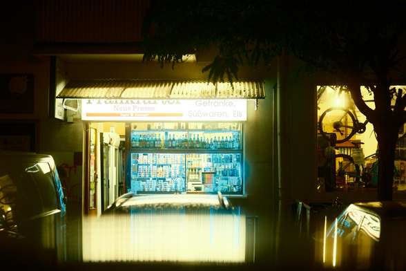 Spannend beleuchtetes Kiosk bei Nacht mit reflection der Beleuchtung auf einem Autodach