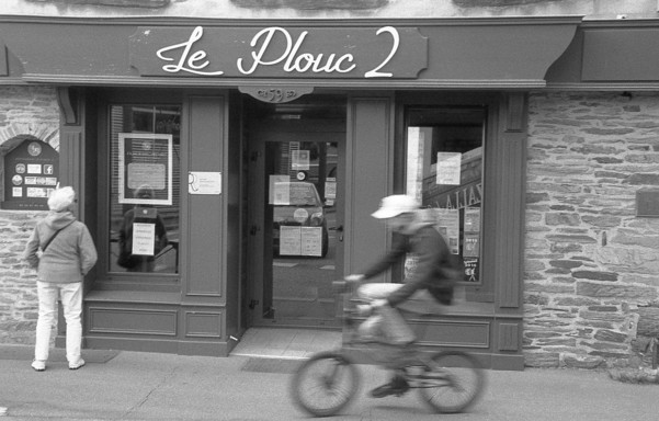 Un vélo passe devant un restaurant, noir et blanc.