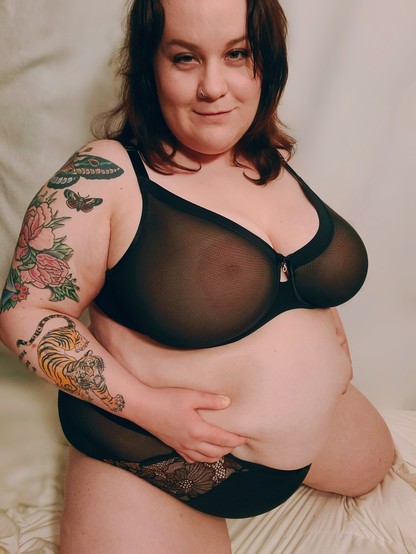 Cat, a bbw, white with curly black hair grabbing her fat belly wearing matching black mesh and lace panties and bra kneeling. She looks at you seductively. 