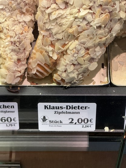 Auslage in der Bäckerei. Man sieht ein Stück von einem Weckmann mit Mandeln und Zuckerguss. Dazu das Etikett „Klaus-Dieter Zipfelmann - 2,00 €“