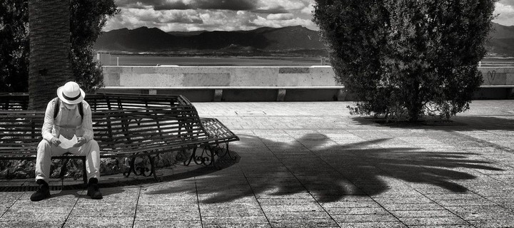 the reminder: a black-and-white photograph of a man sitting on a bench and reading a letter
