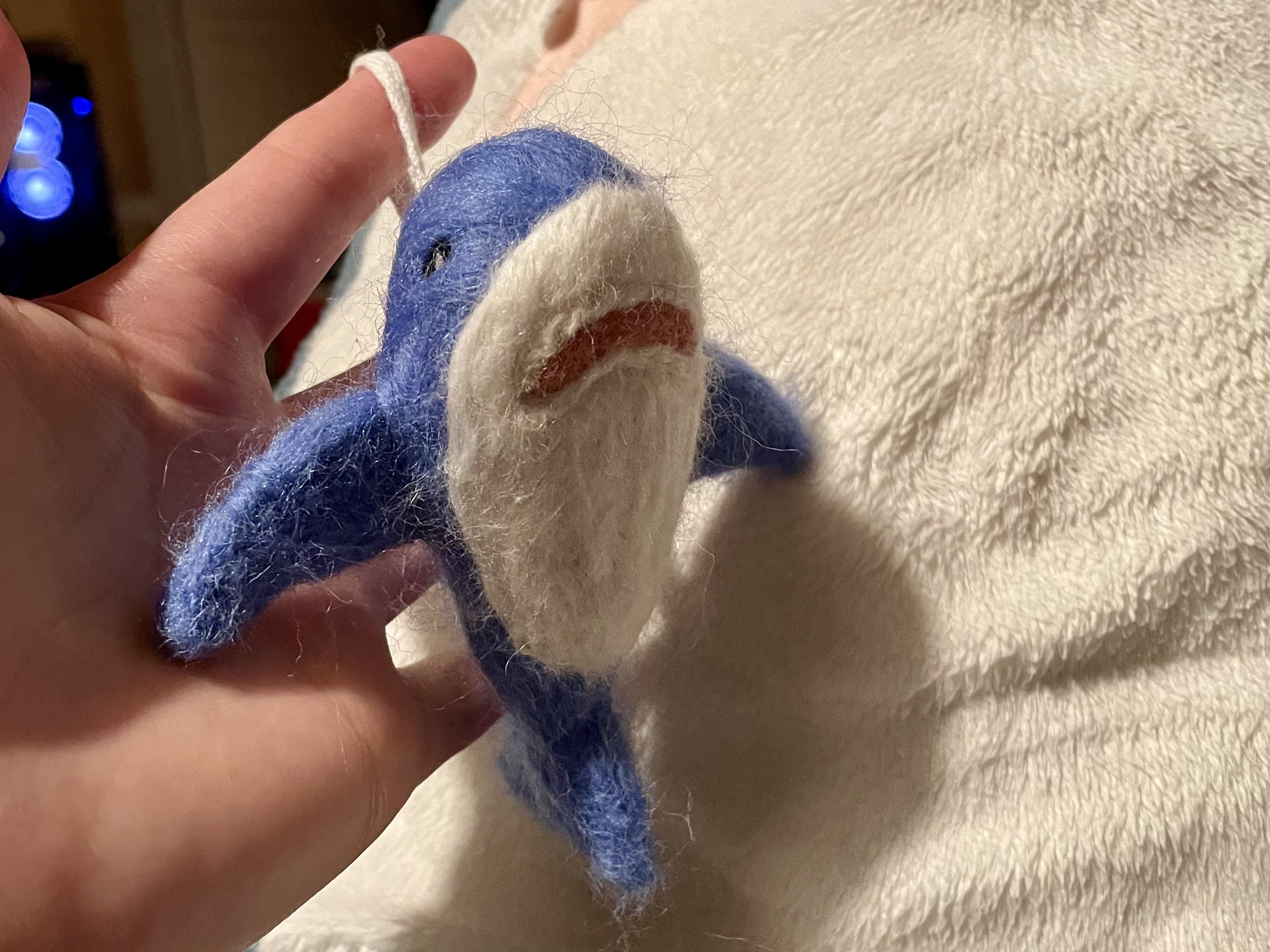 A small blue IKEA shark, known as Blåhaj, made out of wool, hanging on a string in front of its large counterpart.