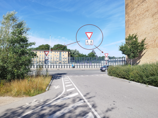 Cross between a bidirectional bicycle path and a road. The give way signal is highlighted and zoomed showing that it has a rectangle indicating graphically that bicycles can come from both ways.