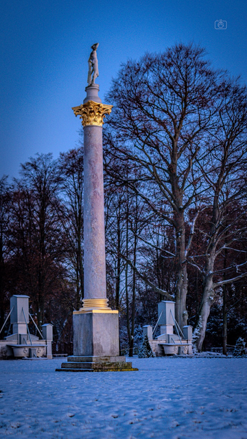 Neoclassical gilded column topped by nymph in snow at dusk, Sanssouci Park, Potsdam, 28 Nov 2023. Nikon D5600, Nikkor DX 35 mm ƒ1.8G, ISO 200, ƒ1.8, -0.3 ev, 1/60s