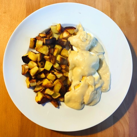 Ein Teller voller Bratkartoffeln und Eiern, die unter dicker Senfsauce versteckt sind