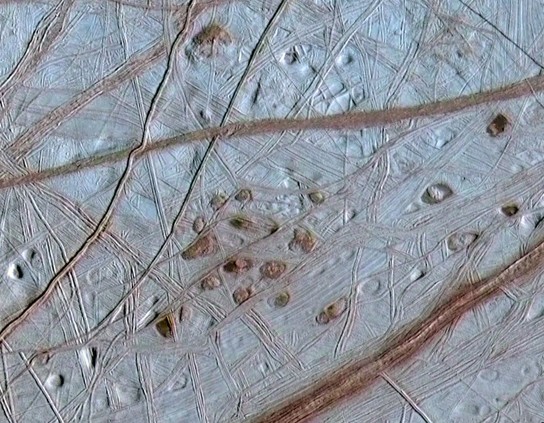 Reddish spots and shallow pits pepper the enigmatic ridged surface of Europa in this view combining information from images taken by NASA's Galileo spacecraft during two different orbits around Jupiter.