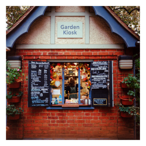 Photo of a woman through the window of coffee shop that looks like a hut called "Garden Kiosk".