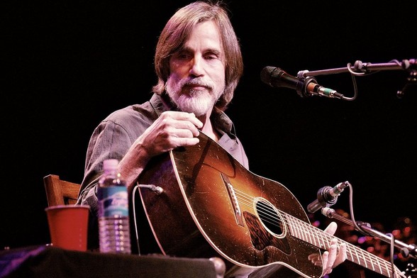 Jackson Browne con barba y su característico flequillo, tocando la guitarra en concierto en una foto relativamente reciente. Craig ONeal • CC BY-SA 2.0
