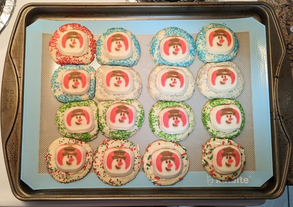 Image shows a pan of sugar cookies with various kinds of sprinkles. The cookies have snowmen on them