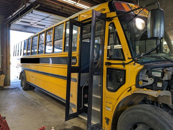 A large school bus is parked inside a garage with about a third of it sticking out the door.