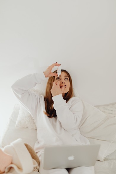 Woman in White Long Sleeves Applying Liquid on Eyes on Bed



