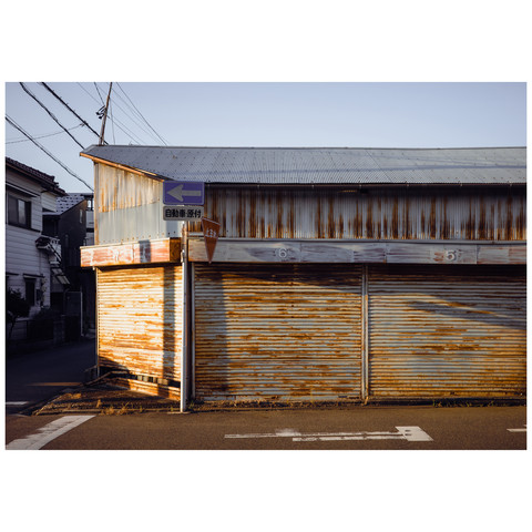 As the sun casts its evening glow, it highlights the sequential dance of numbers on garage doors, their rust-streaked facades a testament to the unyielding progression of time. The warmth of the light bathes the scene in a soft glow, illuminating the metal in hues of gold and amber, capturing a moment of quiet order amid the city's ceaseless rhythm.