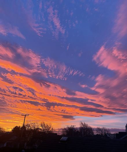 Bright orange sunrise reflected in layers of clouds with blue sky above. Perspective from rooftop. 
