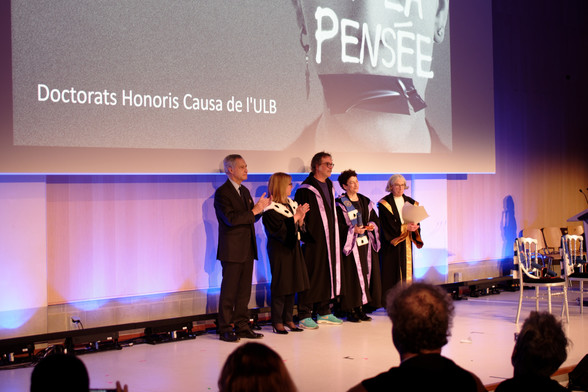 Naomi Oreskes stands on a stage wearing an academic gown, next to academic authorities of Université libre de Bruxelles, also wearing gowns (except for the president of the board) as she receives an honorary doctorate.